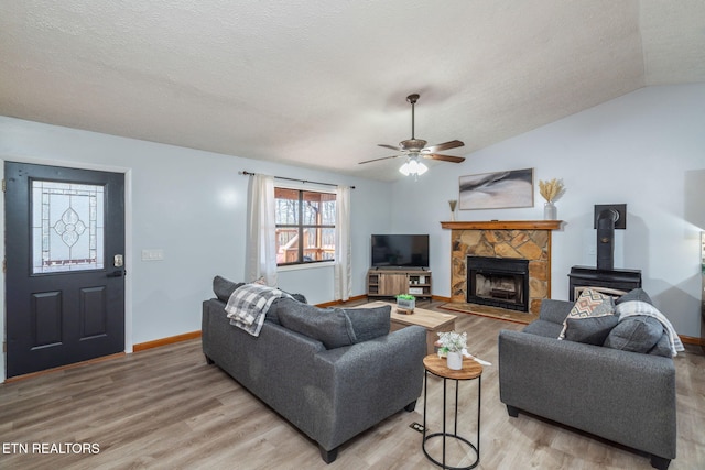 living area featuring a textured ceiling, light wood-type flooring, baseboards, and vaulted ceiling