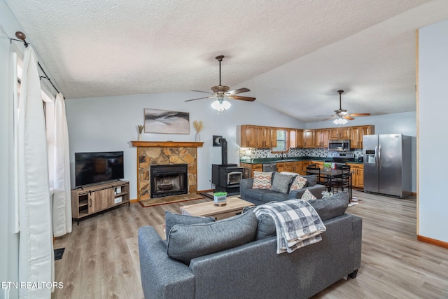 living room featuring vaulted ceiling, a wood stove, light wood finished floors, and a textured ceiling