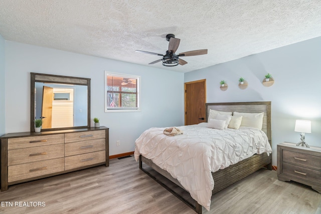 bedroom featuring visible vents, baseboards, light wood-style floors, a textured ceiling, and a ceiling fan