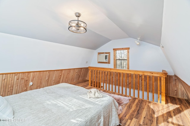 bedroom featuring a wainscoted wall, wood finished floors, wooden walls, and vaulted ceiling