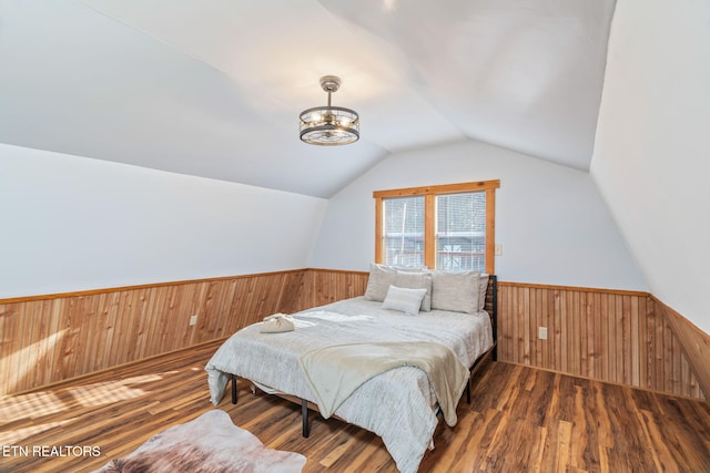 bedroom featuring wainscoting, wood walls, and vaulted ceiling