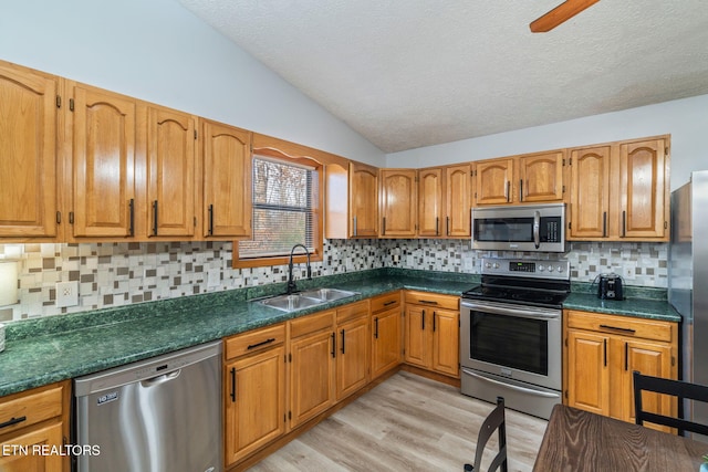 kitchen featuring a sink, dark countertops, appliances with stainless steel finishes, light wood finished floors, and lofted ceiling