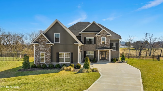 craftsman-style home featuring board and batten siding, a front yard, stone siding, and fence