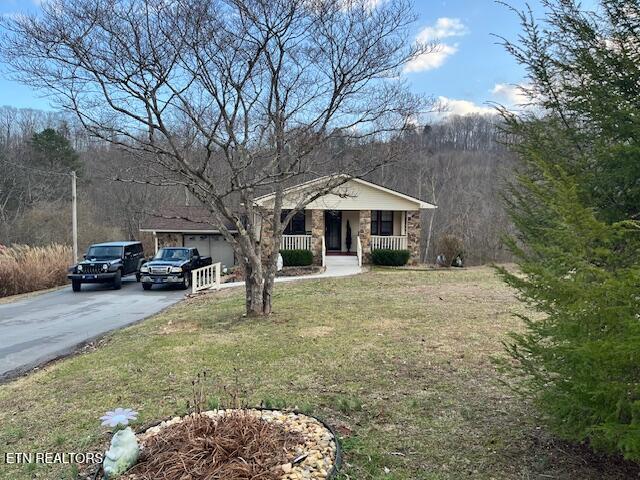 view of front of property with aphalt driveway, covered porch, stone siding, and a front lawn