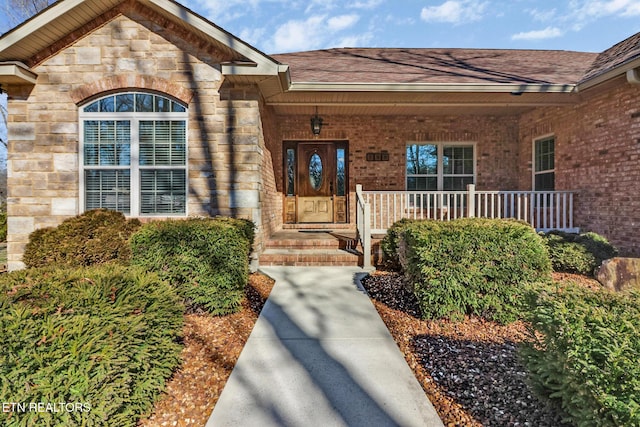 entrance to property with stone siding, brick siding, a porch, and a shingled roof