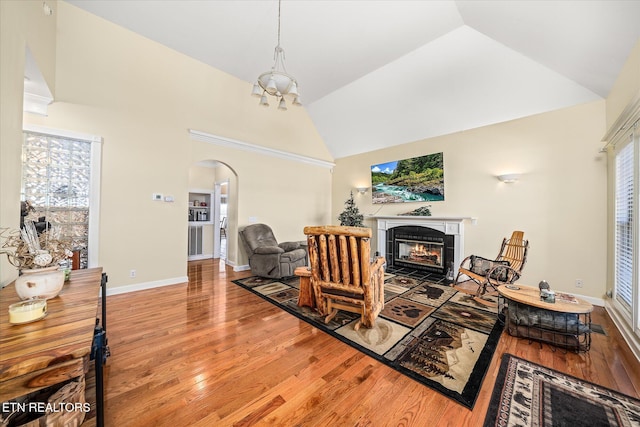 living room with arched walkways, high vaulted ceiling, light wood-style flooring, a fireplace, and baseboards