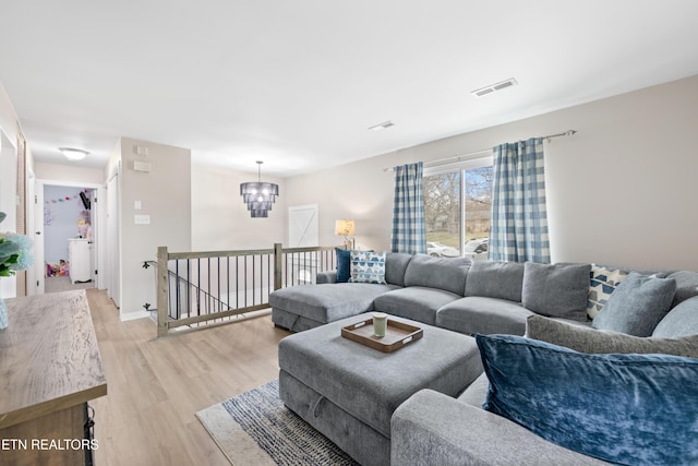 living area featuring light wood-style flooring, a notable chandelier, baseboards, and visible vents