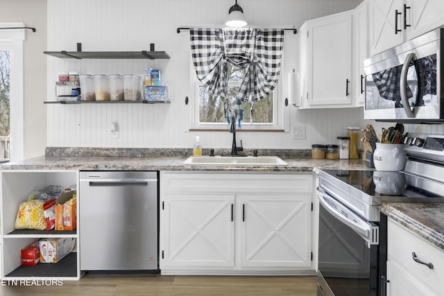 kitchen featuring light wood finished floors, open shelves, stainless steel appliances, white cabinetry, and a sink