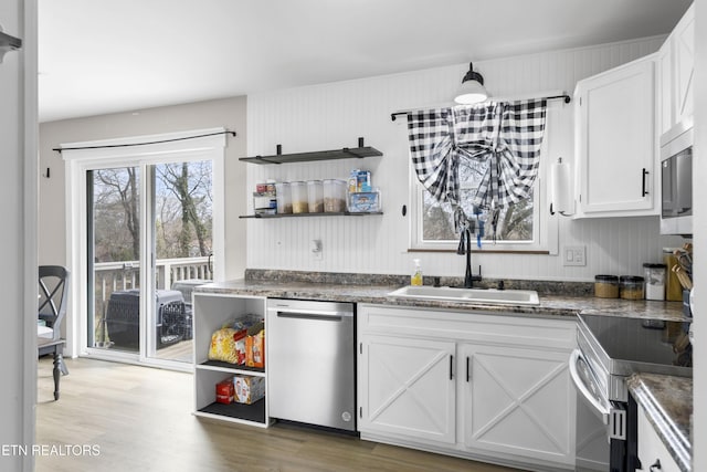 kitchen with a sink, open shelves, wood finished floors, appliances with stainless steel finishes, and white cabinets