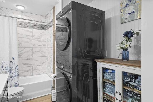 laundry room featuring stacked washer / drying machine, wood finished floors, and laundry area