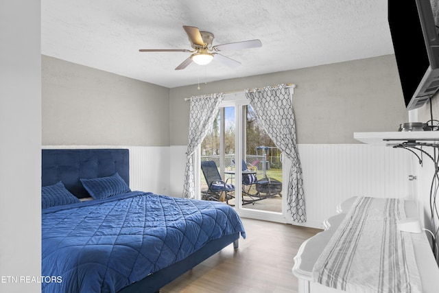 bedroom with wood finished floors, wainscoting, ceiling fan, a textured ceiling, and access to outside