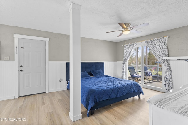 bedroom with light wood-type flooring, a textured ceiling, wainscoting, and access to outside