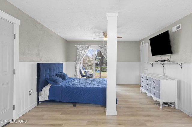 bedroom with a ceiling fan, visible vents, light wood-style flooring, access to exterior, and wainscoting