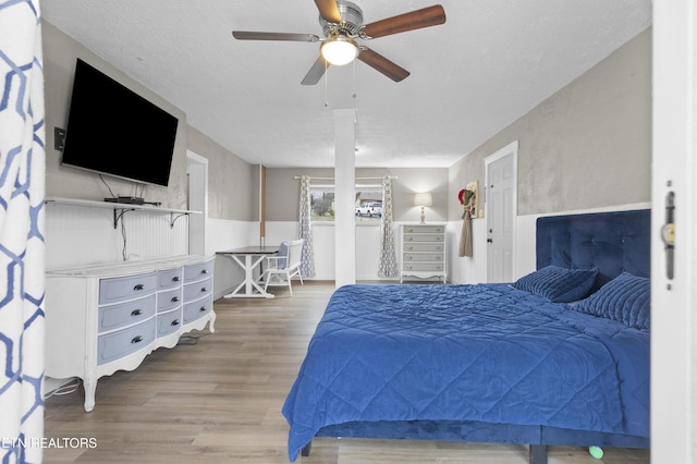 bedroom with wainscoting, a textured ceiling, light wood-style floors, and ceiling fan