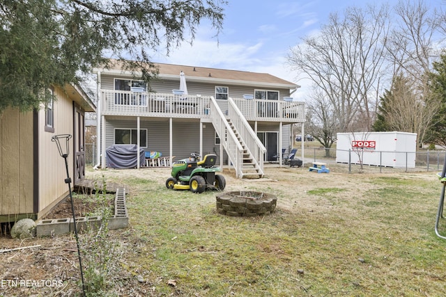 back of property with a fire pit, fence, a wooden deck, stairs, and a lawn