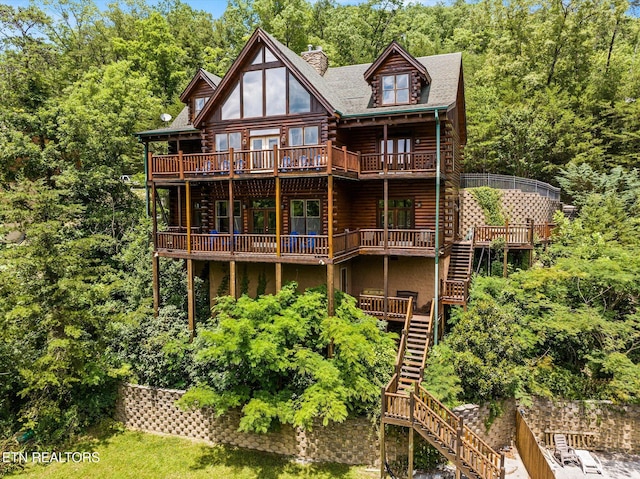 rear view of house with log exterior, a chimney, a wooden deck, and stairs