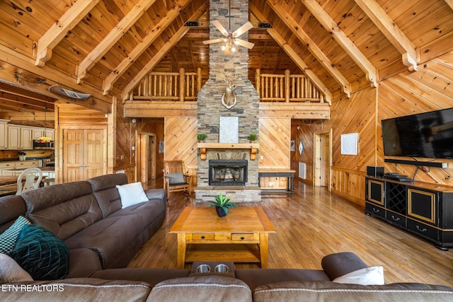 living area featuring vaulted ceiling with beams, wooden walls, a fireplace, wood ceiling, and light wood finished floors