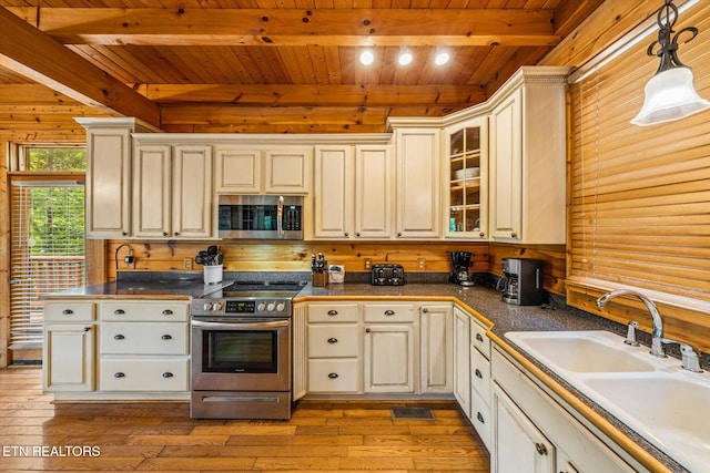 kitchen featuring stainless steel appliances, hanging light fixtures, glass insert cabinets, a sink, and beamed ceiling