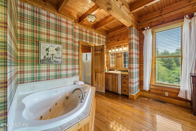 full bath featuring a tub with jets, beamed ceiling, hardwood / wood-style floors, and wallpapered walls