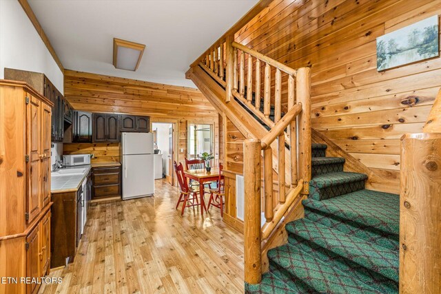 kitchen with wooden walls, white appliances, light wood-style floors, dark brown cabinets, and light countertops