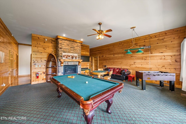 game room with a ceiling fan, carpet, wood walls, and a stone fireplace