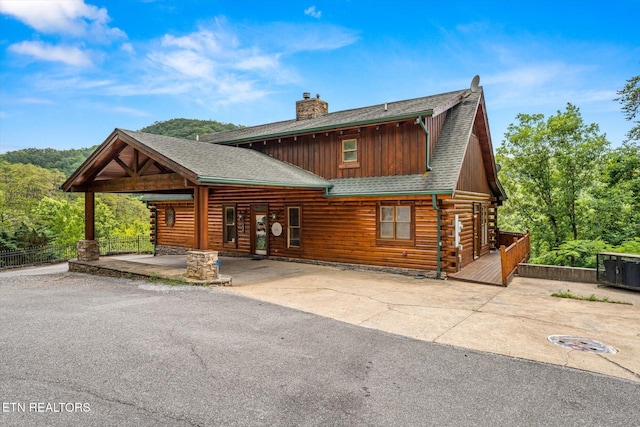 view of front of home with a shingled roof, a chimney, a patio area, and log siding