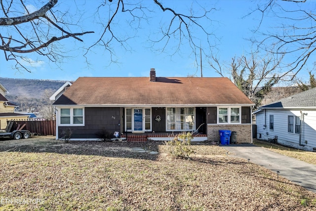 view of front of home with covered porch, a front lawn, a chimney, and fence