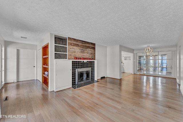 unfurnished living room with a textured ceiling, a fireplace, visible vents, and wood finished floors