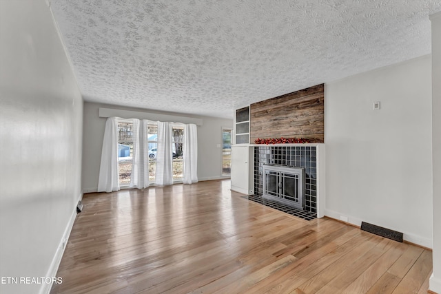 unfurnished living room featuring hardwood / wood-style flooring, a textured ceiling, baseboards, and a tiled fireplace