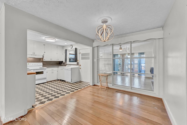 unfurnished dining area with an inviting chandelier, light wood-style floors, a sink, a textured ceiling, and baseboards