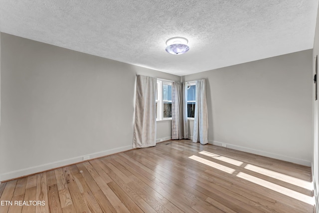 empty room with a textured ceiling, hardwood / wood-style floors, and baseboards