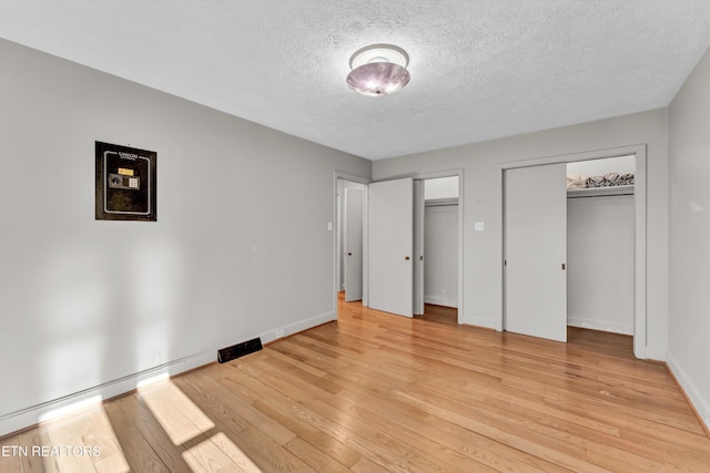 unfurnished bedroom with light wood-style floors, a textured ceiling, baseboards, and multiple closets