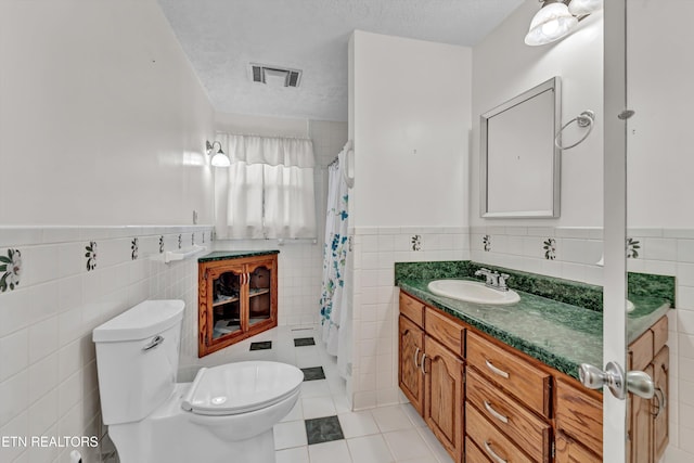 bathroom with a textured ceiling, toilet, visible vents, vanity, and tile walls