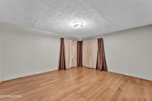 unfurnished room with a textured ceiling, light wood finished floors, and baseboards