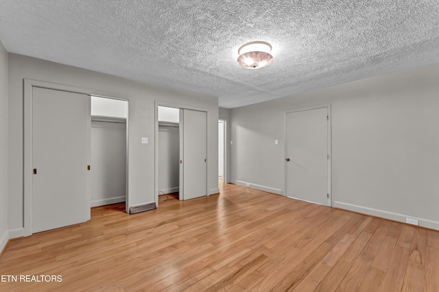 unfurnished bedroom with a textured ceiling, baseboards, light wood-style flooring, and multiple closets