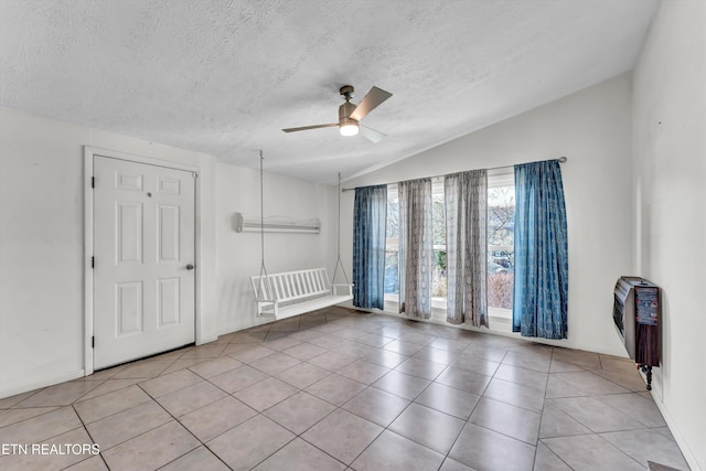 spare room with a ceiling fan, vaulted ceiling, a textured ceiling, and light tile patterned floors