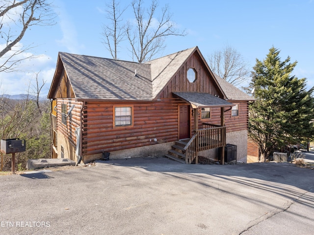 log-style house featuring log exterior, roof with shingles, and driveway