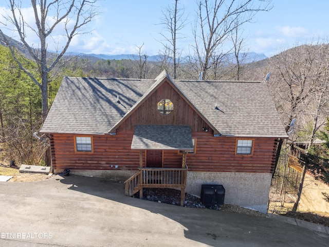 log cabin with log exterior, a shingled roof, and a mountain view