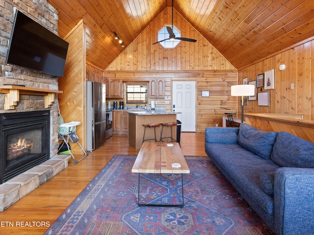 living room with wooden ceiling, wooden walls, wood finished floors, and a stone fireplace