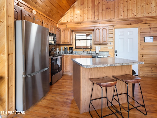 kitchen featuring lofted ceiling, light wood-style flooring, wooden walls, stainless steel appliances, and a sink