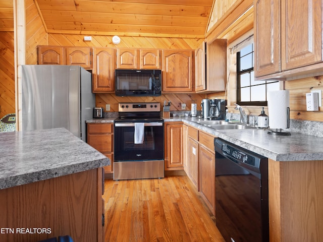 kitchen featuring brown cabinetry, a sink, light wood finished floors, and black appliances