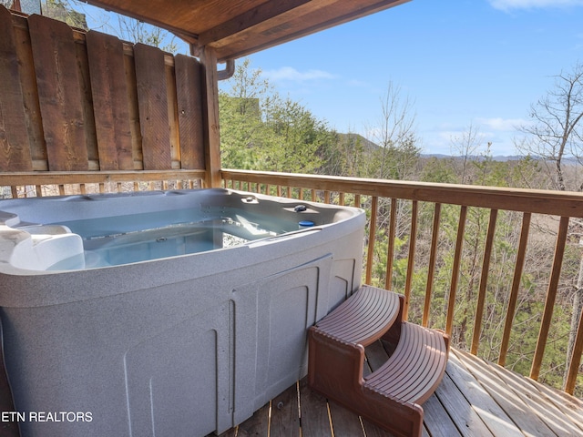 wooden terrace with a wooded view and a hot tub