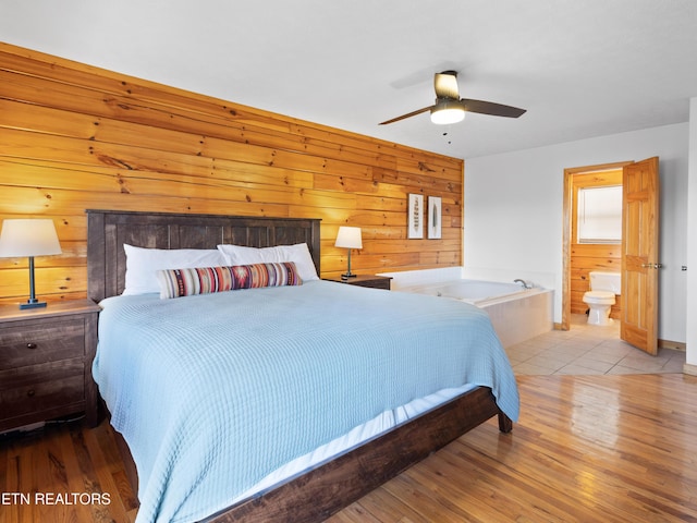 bedroom with a ceiling fan, wood walls, ensuite bathroom, and wood finished floors