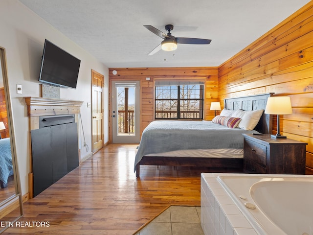 bedroom with access to exterior, light wood-type flooring, a fireplace, and wooden walls