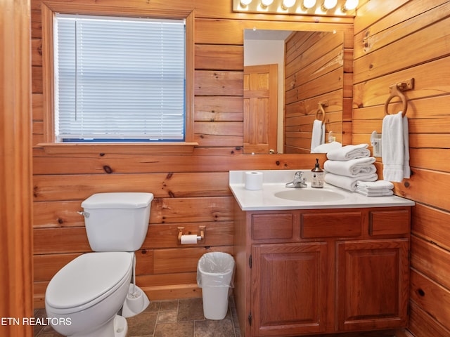 bathroom featuring stone finish floor, vanity, toilet, and wooden walls