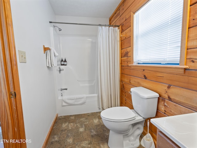 bathroom with shower / tub combo with curtain, toilet, stone finish flooring, wooden walls, and vanity