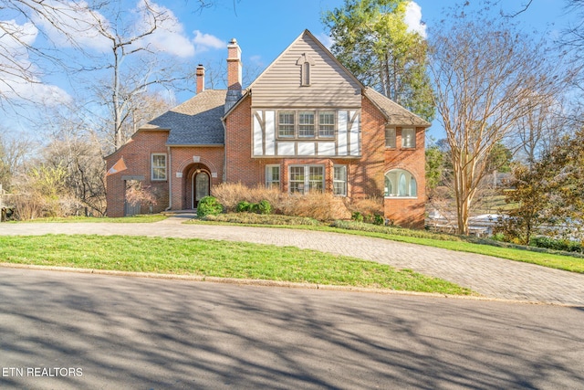 view of front of property with brick siding, a chimney, a shingled roof, a front yard, and driveway