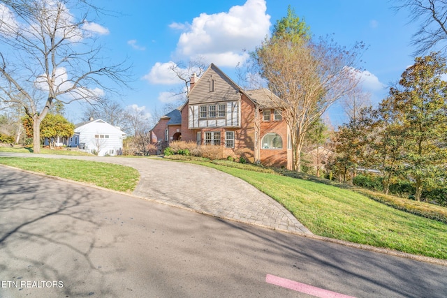 view of front of house with decorative driveway, brick siding, a chimney, and a front lawn