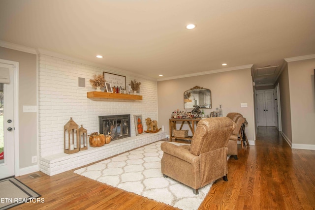 living area featuring crown molding, a fireplace, visible vents, and wood finished floors