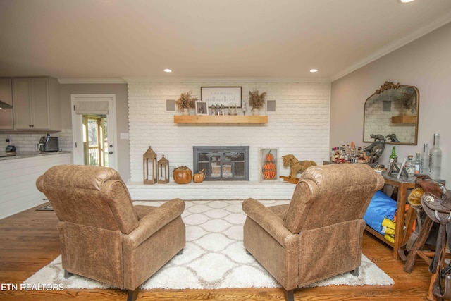 living area featuring recessed lighting, brick wall, wood finished floors, a brick fireplace, and crown molding